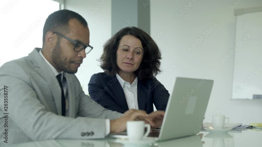 Side view of office employees sitting at table and using laptop. Handsome young businessman typing on laptop with colleague nearby. Business meeting concept Side view of office employees sitting at table and using laptop. Handsome young businessman typing on laptop with colleague nearby. Business meeting concept