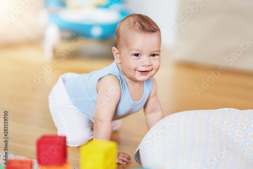 Cute smiling baby boy crawling on floor in living room