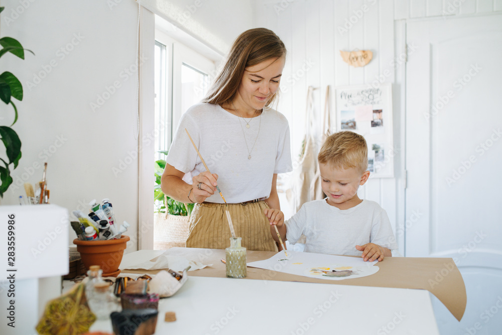 Young mother and first grade son are painting together at home