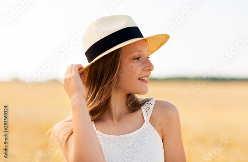 nature, fashion and people concept - portrait of smiling young girl in straw hat on cereal field in summer