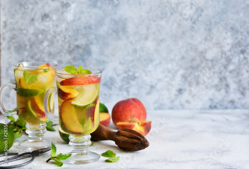 Cold summer drink with peach, lime and mint on a concrete background.