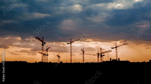 Time-lapse view on a consturction site with cranes during sunset with stormy clouds.