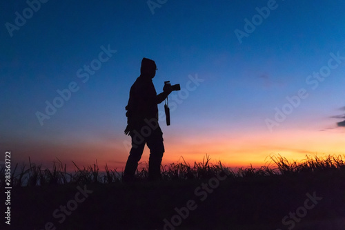 Silhouette of man taking pictures with his camera while sunset hour; against twilight sky over a mountain. Traveling and vacation concept.