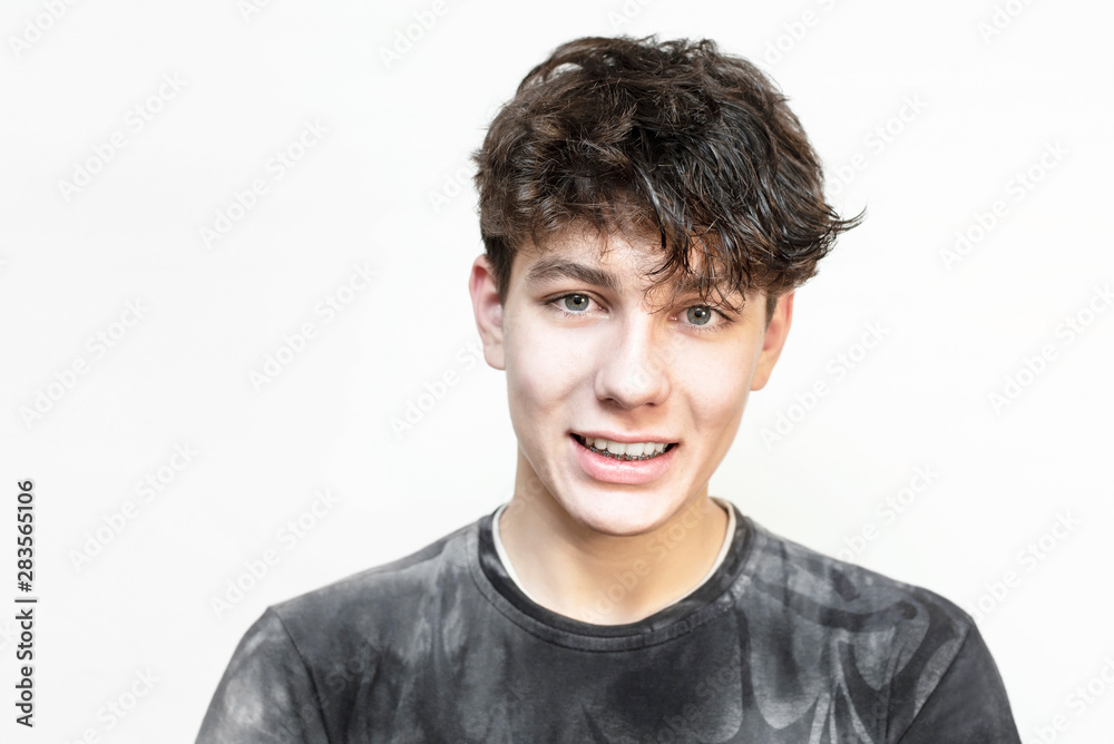 A teenage boy smiles against a light background in a dark T-shirt, showing that he has braces on his lower jaw A teenage boy smiles against a light background in a dark T-shirt, showing that he has braces on his lower jaw