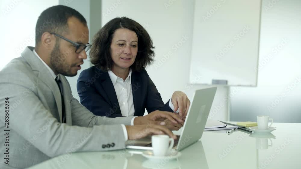 Joyful office employees sitting at table and using laptop. Handsome young businessman typing on laptop with colleague nearby. Business meeting concept Joyful office employees sitting at table and using laptop. Handsome young businessman typing on laptop with colleague nearby. Business meeting concept