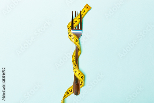 Close up of fork wrapped with tape measure on blue background. Top view of obesity concept photo