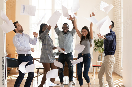 Overjoyed multiracial business team people tossing papers dancing in office photo