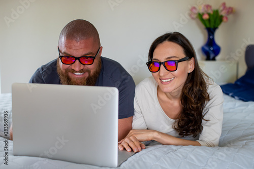 Fotografi Happy couple relaxing at home with lap top, looking at the screen with orange bl