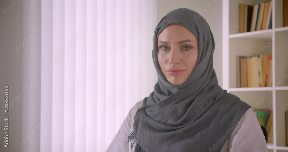 Closeup portrait of young attractive muslim businesswoman in hijab looking at camera smiling cheerfully in office indoors Closeup portrait of young attractive muslim businesswoman in hijab looking at camera smiling cheerfully in office indoors