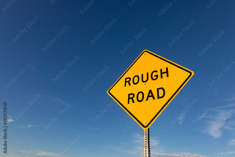 Isolated closeup looking up at yellow rough road warning sign with blue sky and white clouds in background. Copy space Isolated closeup looking up at yellow rough road warning sign with blue sky and white clouds in background. Copy space