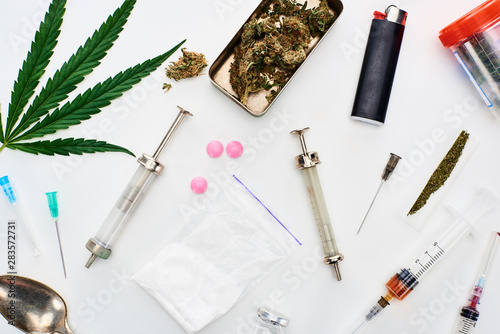 top view of marijuana buds, cannabis leaf, heroin, lsd and syringes on white background