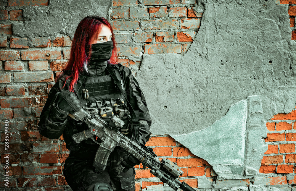 Airsoft red-hair woman in uniform with machine gun beside brick wall ...