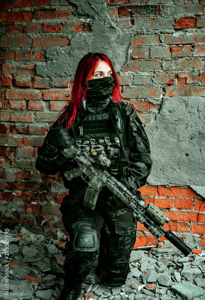 Airsoft Red-hair woman in uniform with machine gun standing on one knee ...