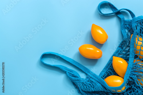 Fresh yellow tomatoes in a cotton string bag on a blue background Fototapet
