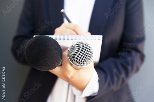 Female journalist at news conference or media event, writing notes, holding microphone