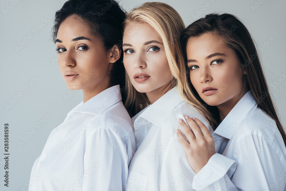 three attractive multiethnic girls in white shirts embracing isolated on grey three attractive multiethnic girls in white shirts embracing isolated on grey