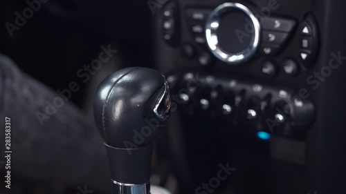 Close-up of female driver hand switching automatic transmission in luxury car before driving. Black car interior view, woman sitting on driver's seat shifting gear knob going to drive car photo