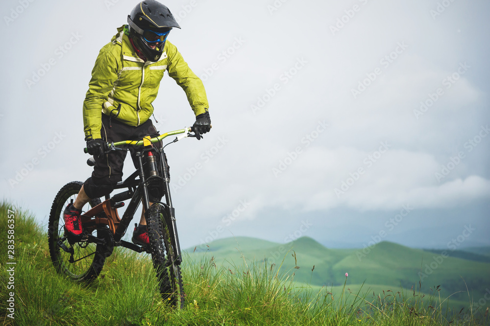 Front view of a man on a mountain bike standing on a rocky terrain and looking down against a gray sky. The concept of a mountain bike and mtb downhill Front view of a man on a mountain bike standing on a rocky terrain and looking down against a gray sky. The concept of a mountain bike and mtb downhill