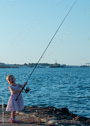 Pretty little girl "fisherwoman" with a ultralight spinning on summer sea fishing. Positive person. Beautiful smiling young woman. Happy childhood.