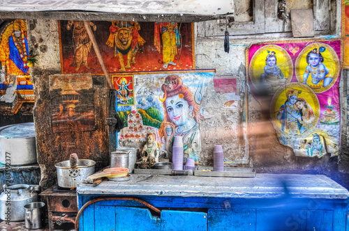 Chai tea street food stall with posters of shiva the god on the wall and a blurry person walking by in Delhi India