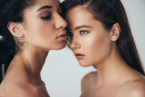 two attractive nude multiethnic young women looking away isolated on grey