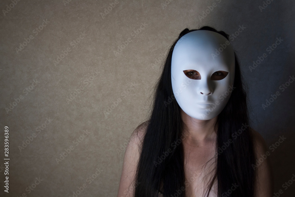 Masked young woman sitting in a dark room Masked young woman sitting in a dark room