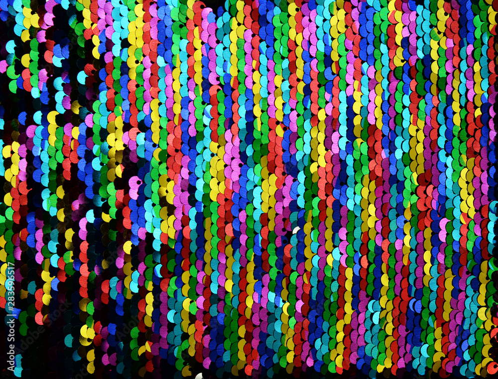 Sequins close-up macro. Abstract background with multicolor sequins on the fabric. Texture scales of round rainbow sequins with color transition.