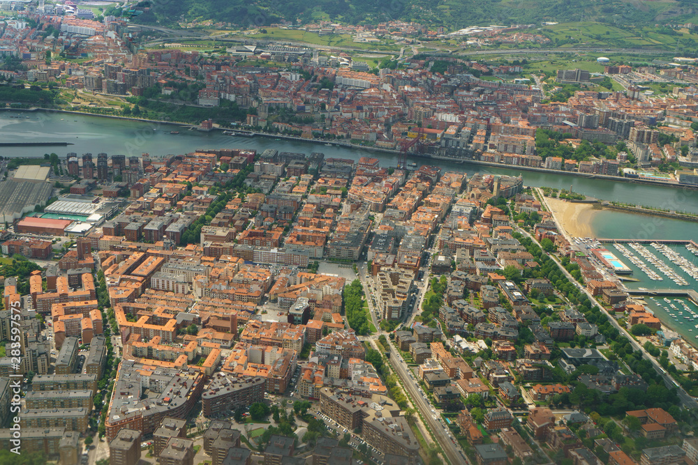 Aerial view from the aircraft window of Bilbao surrounding area. Photography of houses roofs, river and roads in Basque country in summer day. Photo is suitable for greeting card, postcard, poster.