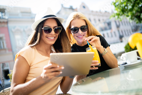 Holidays, tourism and internet - beautiful girls looking at tablet pc in cafe outside