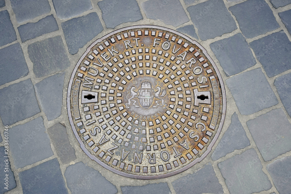 Cast iron ornamented manhole cover in Budapest, Hungary. Closeup of duct  manhole cover with Budapest Coat of Arms at the Old Town district. Sewerage hatchway. Selective focus. Copy space