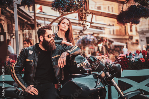 Beautiful couple with brutal biker and his sexy gilfriend are chilling near cefeteria with motorbike.