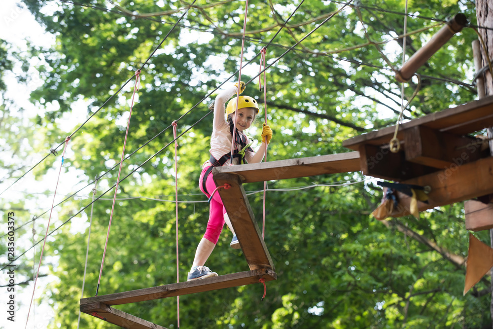 Enjoy childhood years. Happy little girl in summer. Playground. Cargo net climbing and hanging log. Cute school little girl enjoying a sunny day in a climbing adventure activity park. Enjoy childhood years. Happy little girl in summer. Playground. Cargo net climbing and hanging log. Cute school little girl enjoying a sunny day in a climbing adventure activity park.