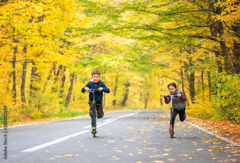two kids with scooter on the autumn street two kids with scooter on the autumn street