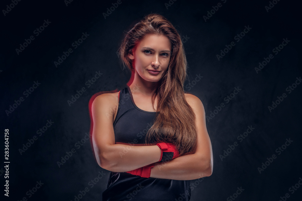 Physically fit woman with long hair is standing crossed her hands over dark background.