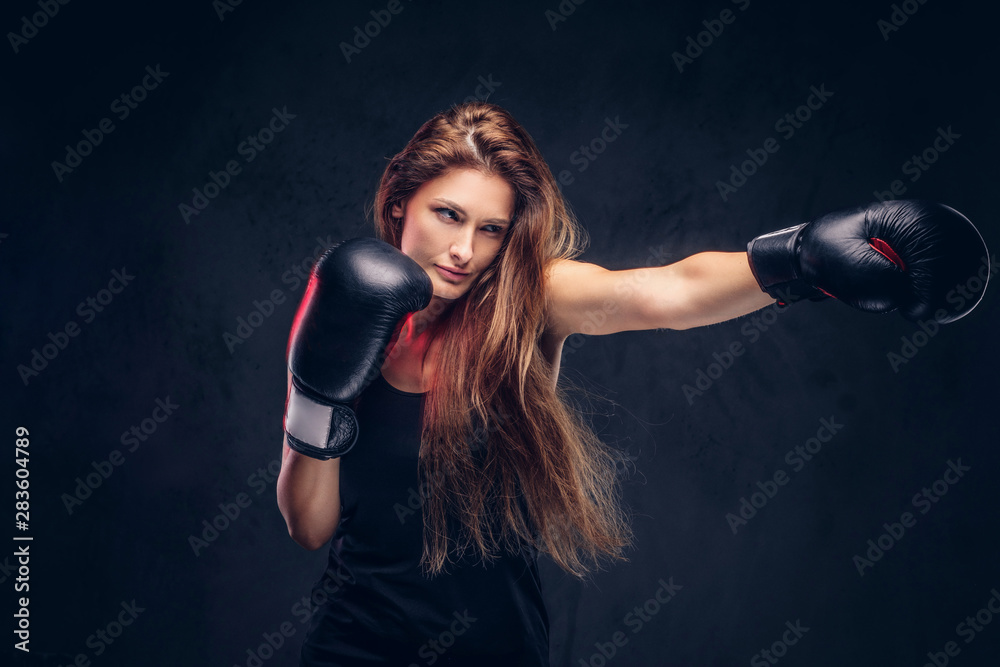 Beautiful woman with long hair is demonstraiting her hit at studio. She is wearing boxing gloves.