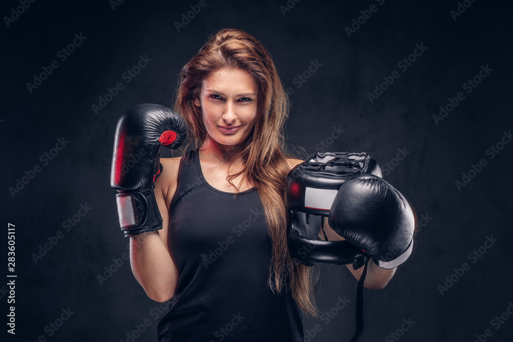 Happy smiling woman wearing boxer gloves is holding protective helmet at studio.