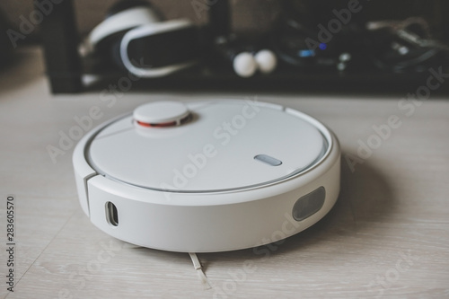 A robot vacuum cleaner removes debris on a laminate. Smart cleaning. White robotic vacuum cleaner.