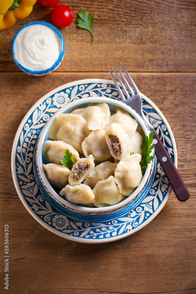 Pierogi or pyrohy, varenyky, vareniki - dumplings in bowl served with sour cream or yogurt on wooden table Pierogi or pyrohy, varenyky, vareniki - dumplings in bowl served with sour cream or yogurt on wooden table