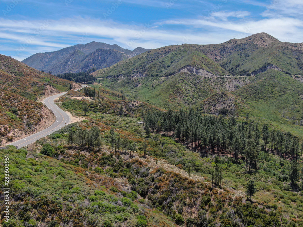 Fototapeta premium Asphalt road bends through Angeles National forests mountain, California, USA. Thin road winds between a ridge of hills and mountains at high altitude