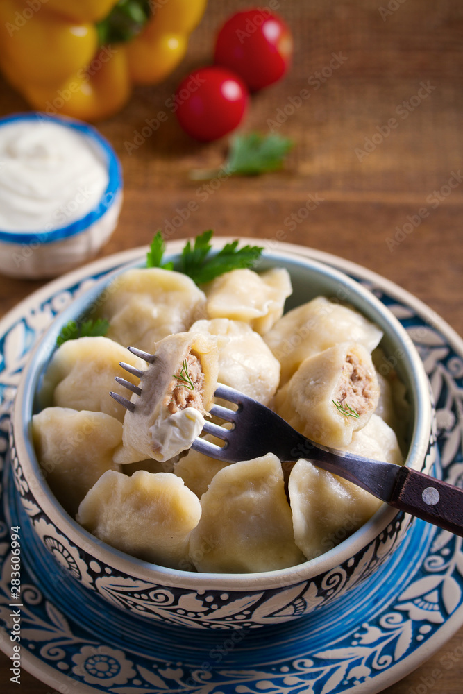 Pierogi or pyrohy, varenyky, vareniki - dumplings in bowl served with sour cream or yogurt on wooden table