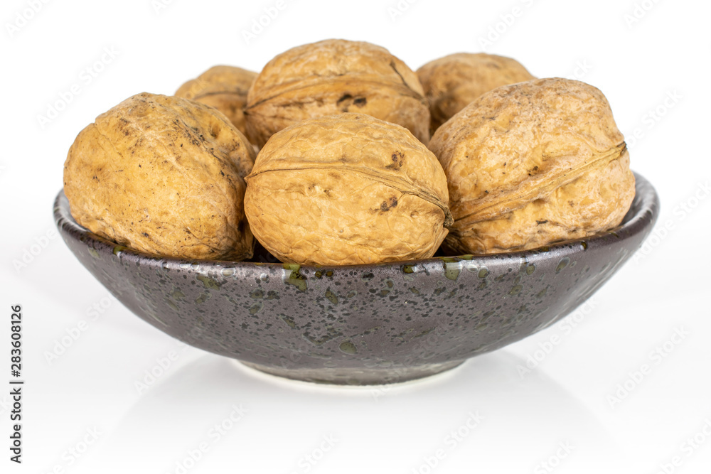 Lot of whole ripe brown walnut in dark ceramic bowl isolated on white background Lot of whole ripe brown walnut in dark ceramic bowl isolated on white background