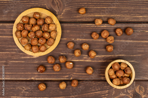 Lot of whole ripe brown hazelnut on round bamboo coaster in tiny wooden bowl flatlay on brown wood