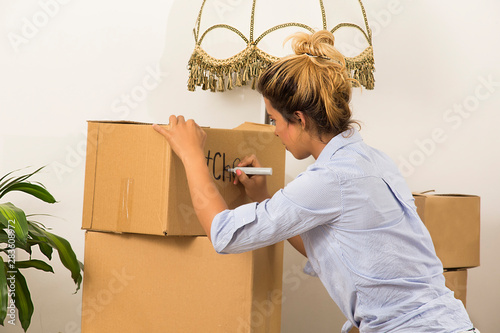 Young woman kneeling marking the cardboard boxes with her belongings for her transfer.