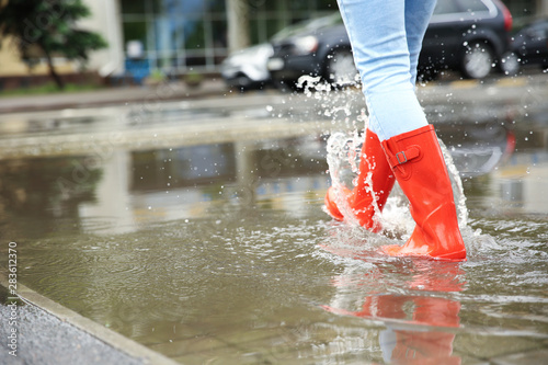 Woman with red rubber boots in puddle, closeup. Rainy weather
