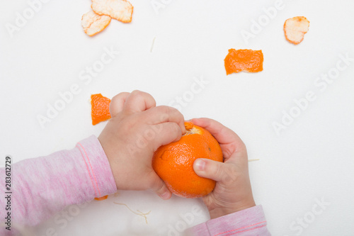 children's hands peel mandarin on a white background pink orange