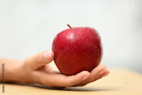 Woman holding fresh red apple at table, closeup