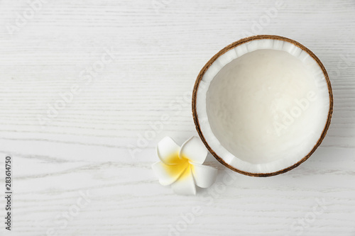 Half of coconut and flower on white wooden background  top view. Space for text