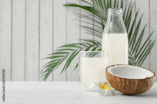 Composition with bottle and glass of coconut water on white wooden table. Space for text