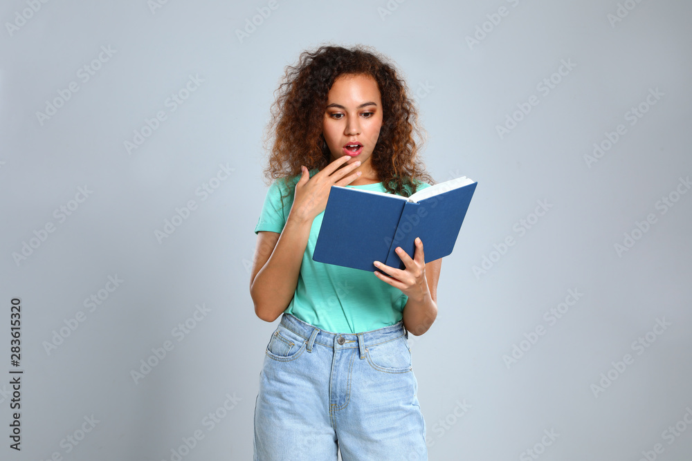 Beautiful African-American young woman reading book on light background Beautiful African-American young woman reading book on light background