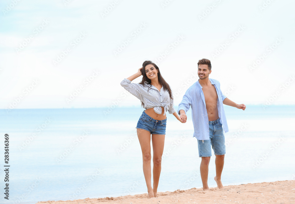 Happy young couple walking together on beach near sea